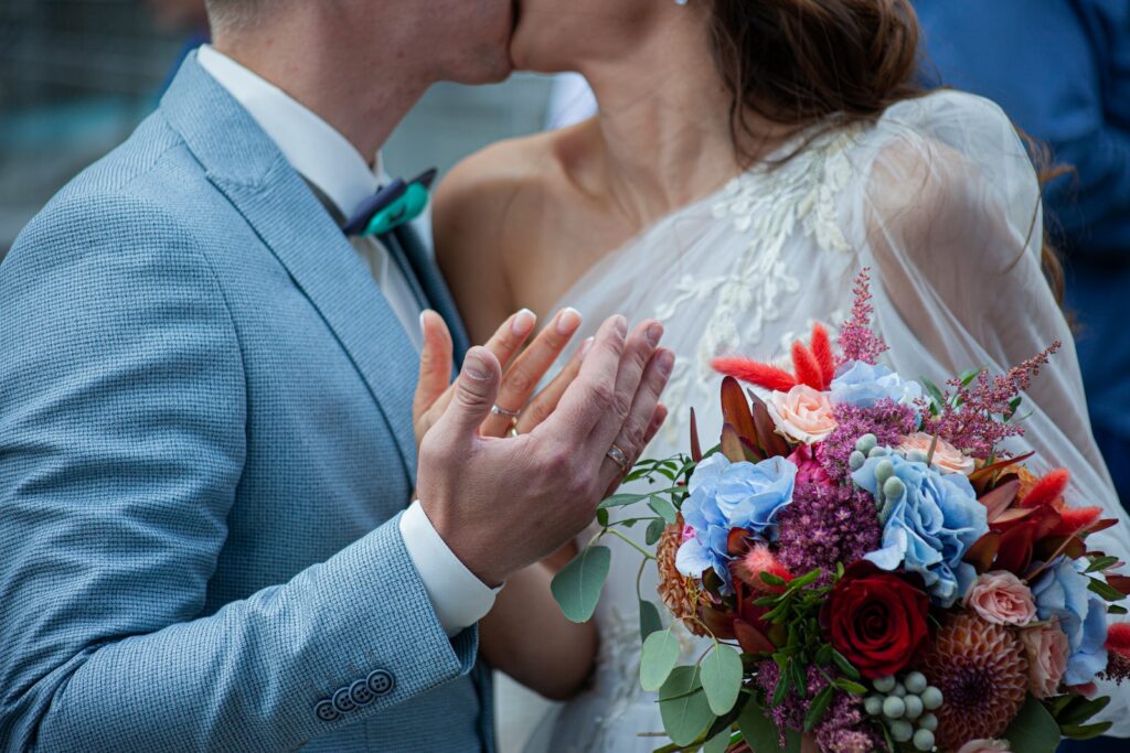 Mann in grauer Anzugjacke hält Frau in weißem Hochzeitskleid